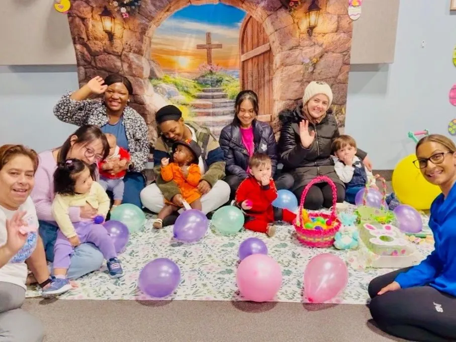 Parents and young children sit on a carpet with balloons and Easter activities