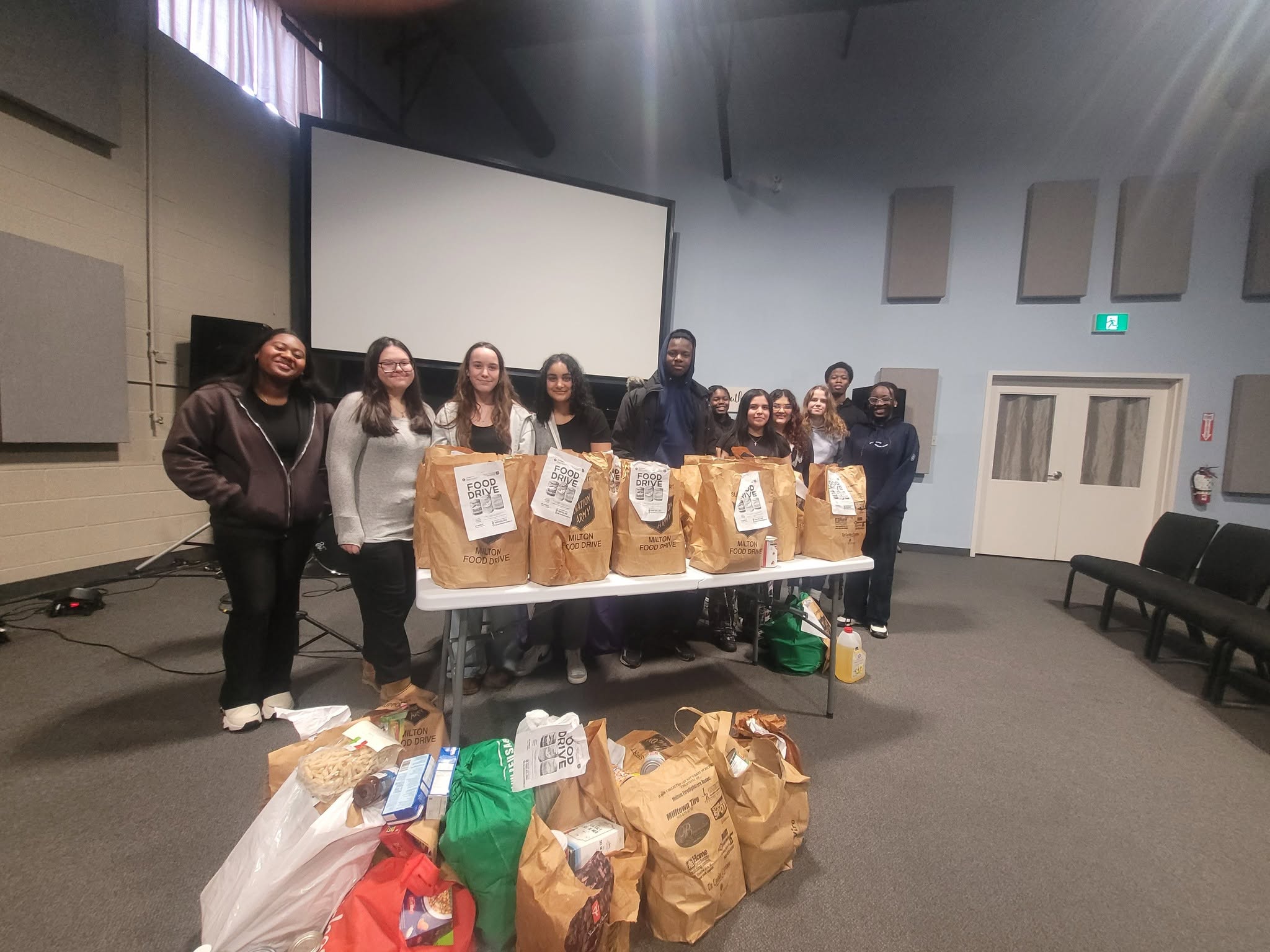 Eleven teenagers pose in front of bags of donated goods from a food drive